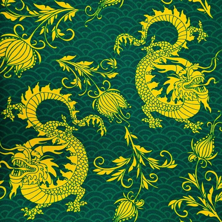 A close up of polyester and silk fabric with a print of golden yellow dragons and flowers with light green sea swirls on a dark rich green background.