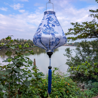 Blue and white teardrop shaped lantern with blue tassel hanging outdoors against a natural background