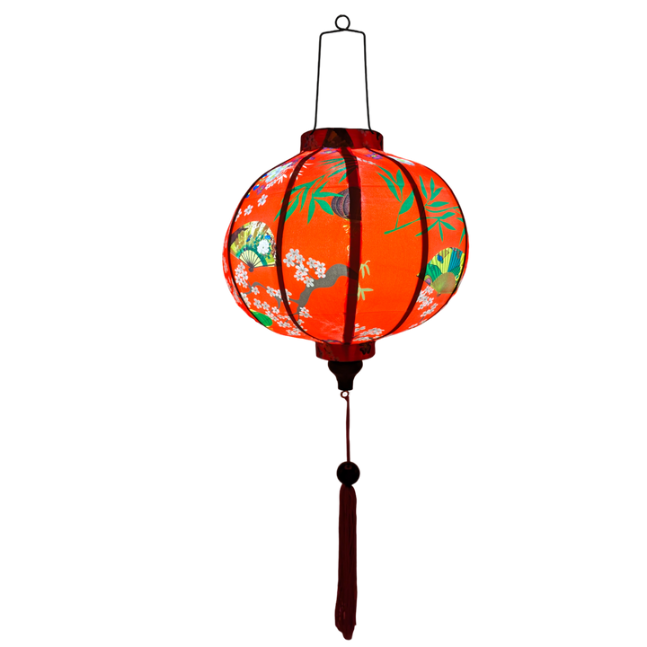 Glowing Round Vietnamese lantern with red tassel with black, yellow and green lanterns and multi colour fans surrounded by white cherry blossoms on a bold red background.