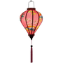 Glowing Balloon shaped Vietnamese Hoi An Lantern with pink tassel  and a design of yellow fans, a house overlooking trees beneath snow capped mountains and surrounded by blooms of pink on a brilliant pink background. 