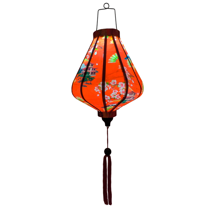 Glowing Teardrop shaped Vietnamese lantern with red tassel and design of yellow fans, a house overlooking trees beneath snow capped mountains and surrounded by blooms of pink on a brilliant red background. 