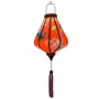 Glowing Teardrop shaped Vietnamese lantern with red tassel and design of yellow fans, a house overlooking trees beneath snow capped mountains and surrounded by blooms of pink on a brilliant red background. 