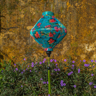 Lozenge shaped lantern hanging in Old Town, Hoi An with a yellow wall and purple flowers in the background.