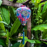 A Balloon shaped lantern with floral design on a blue background hanging in a garden setting.