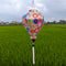 Balloon shaped lantern outdoors hanging in front of rice field in Hoi An featuring an illustration of different colour flowers on white background.