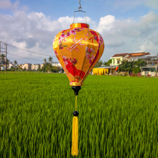 Balloon shaped lantern with flowers, fans and bamboo design hanging over a green rice field in Hoi An.