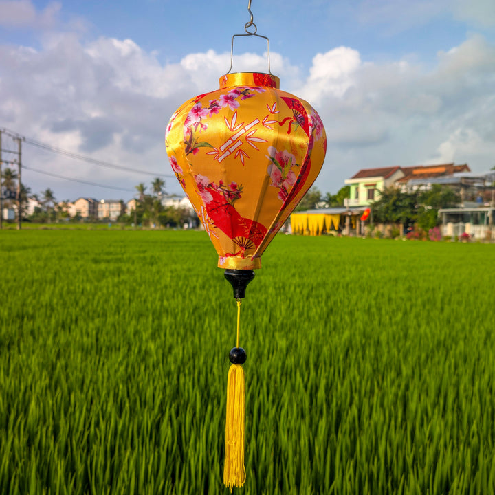 Balloon shaped lantern with flowers, fans and bamboo design hanging over a green rice field in Hoi An.