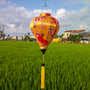 Balloon shaped lantern with flowers, fans and bamboo design hanging over a green rice field in Hoi An.