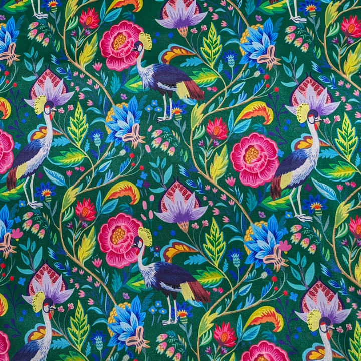 Close up of polyester silk fabric featuring a print of lush, tropical flowers and birds on a deep green silk fabric. 