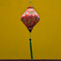 Lozenge Vietnamese lantern with delicate chrysanthemum flowers in yellow, green, brown hanging in front of a bright yellow temple wall. 
