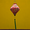 Lozenge Vietnamese lantern with delicate chrysanthemum flowers in yellow, green, brown hanging in front of a bright yellow temple wall. 