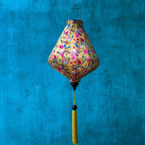 Teardrop shaped lantern with floral pattern and yellow tassel against a blue background