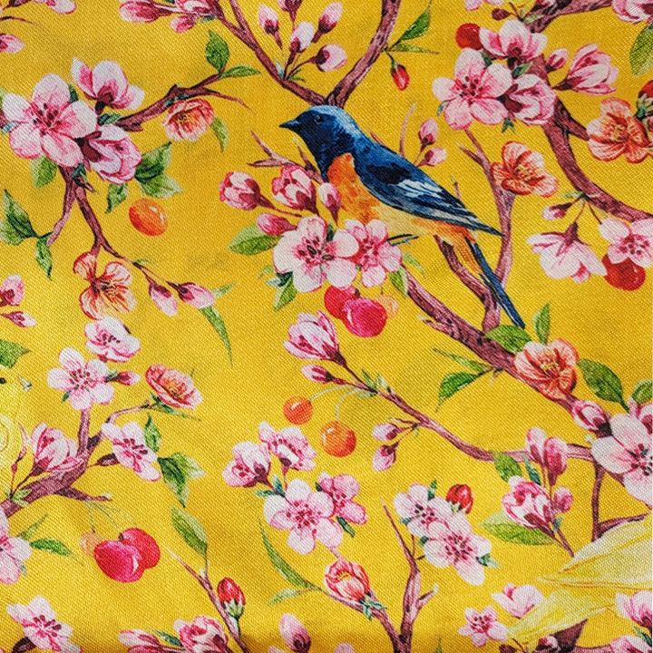 Polyester silk fabric with yellow and bright blue and orange flycatcher birds sitting in a cherry tree. The cherry tree is bursting with pink flowers and red berries, set against a sunny yellow background. 