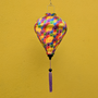 Colourful hanging balloon shaped lantern with fractal floral pattern against a yellow wall with purple tassel