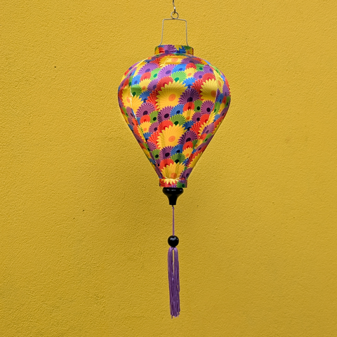 Colourful hanging balloon shaped lantern with fractal floral pattern against a yellow wall with purple tassel