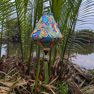 Teardrop shape Vietnamese silk lantern featuring a stunning paisley print with red, greens, blues and yellows hanging in front of a river in Cam Thanh.