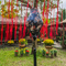 Tube shaped Vietnamese Hoi An Lantern in a garden setting with red ribbons and pretty yellow flowers.