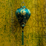 A balloon shaped lantern with a print of yellow dragons on dark green background hanging in front of a textured, cracked yellow and green wall.