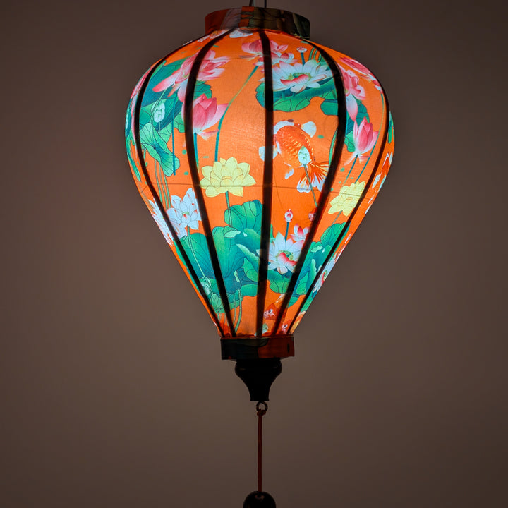 Glowing balloon shaped lantern with goldfish and lotus flowers on a orange background