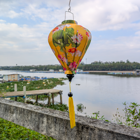 Balloon shaped lantern with lotus flowers and fish design hanging near a river 