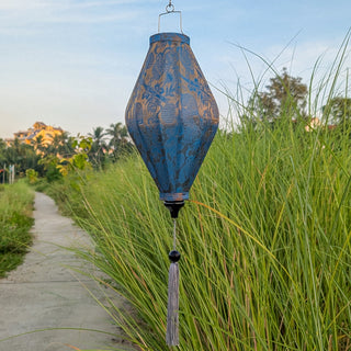 Teal and gold jacquard silk lantern in tube shape with tassel hanging in tall grass 
