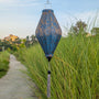 Teal and gold jacquard silk lantern in tube shape with tassel hanging in tall grass 