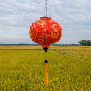 Orange lantern with gold patterns hanging over a rice field