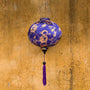 Round purple lantern with gold dragons print hanging in front of a textured old wall in Hoi An