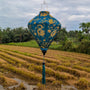 Diamond shaped Vietnamese silk lantern in a teal green with golden yellow dragons hanging over a rice field.