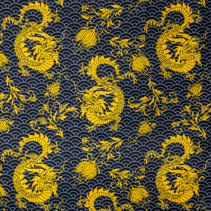 Close up of polyester silk fabric with a print of golden yellow dragons and flowers set against a grey sea pattern of swirls on a rich black background.