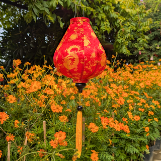 Red lantern with gold dragon design hanging among orange flowers and green foliage