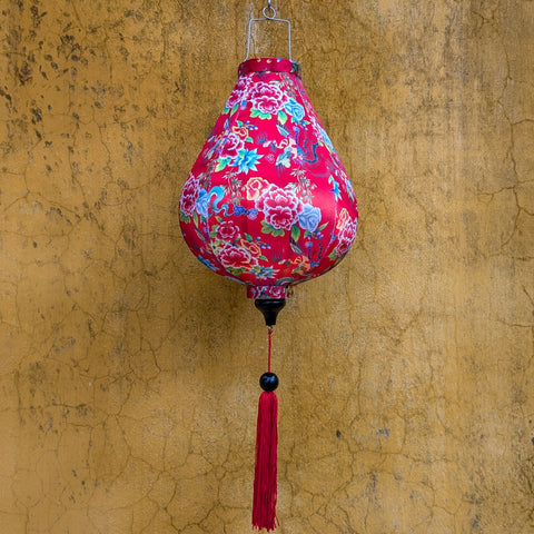 Garlic shaped lantern with little green dragons, flowers and red tassel against a temple wall