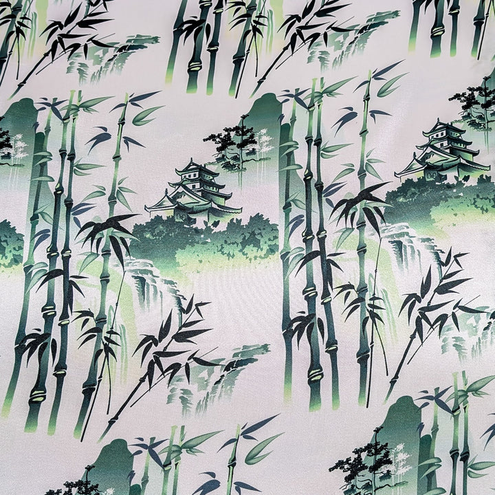 Polyester silk fabric features a green print of pagodas and temples above misty hilltops with large bamboo trees. 