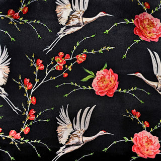 A close up of polyester silk fabric featuring a print of herons in flight surrounded by pink flowers on black background.