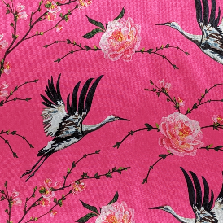 Close up of polyester silk fabric with large herons flying amongst pink roses on a bright pink background.