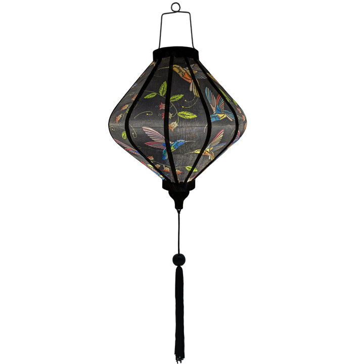 Glowing Lozenge shaped Lantern with colourful cross stitched hummingbirds in flight amongst blue bell flowers and bright green leaves on black.