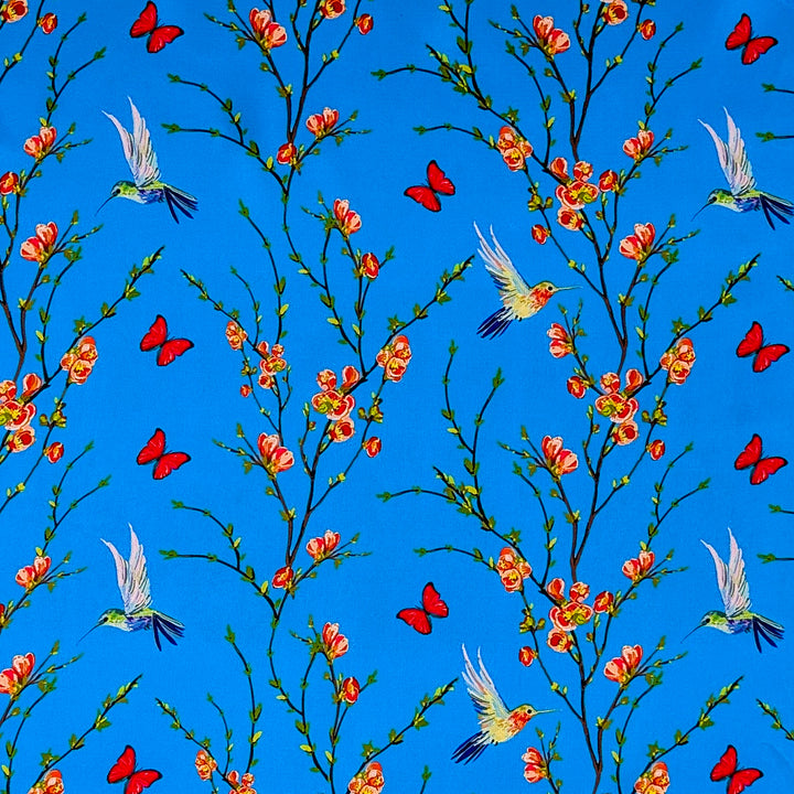 Polyester silk fabric featuring a print of hummingbirds in flight with red and pink flowers against bright blue silk. Used to create Vietnamese silk lanterns in Hoi An.