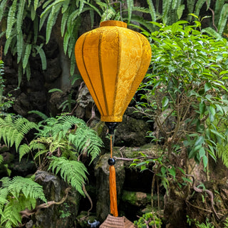 Mustard yellow lantern with tassel hanging among green foliage