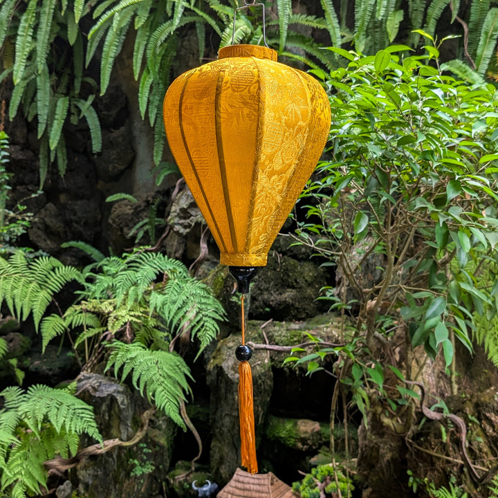 Mustard yellow lantern with tassel hanging among green foliage