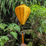 Mustard yellow lantern with tassel hanging among green foliage