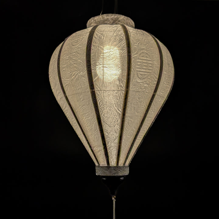 Glowing Hoi An silk lantern in a balloon shape, crafted from luxurious white jacquard fabric with intricate floral patterns woven into the material. 