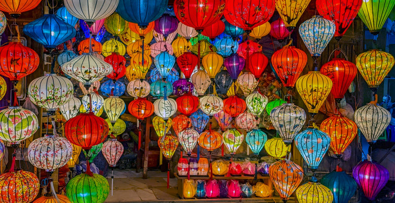 A store front of authentic handmade Vietnamese lanterns lit up and glowing, in a large variety of bright beautiful colours, shapes and sizes.