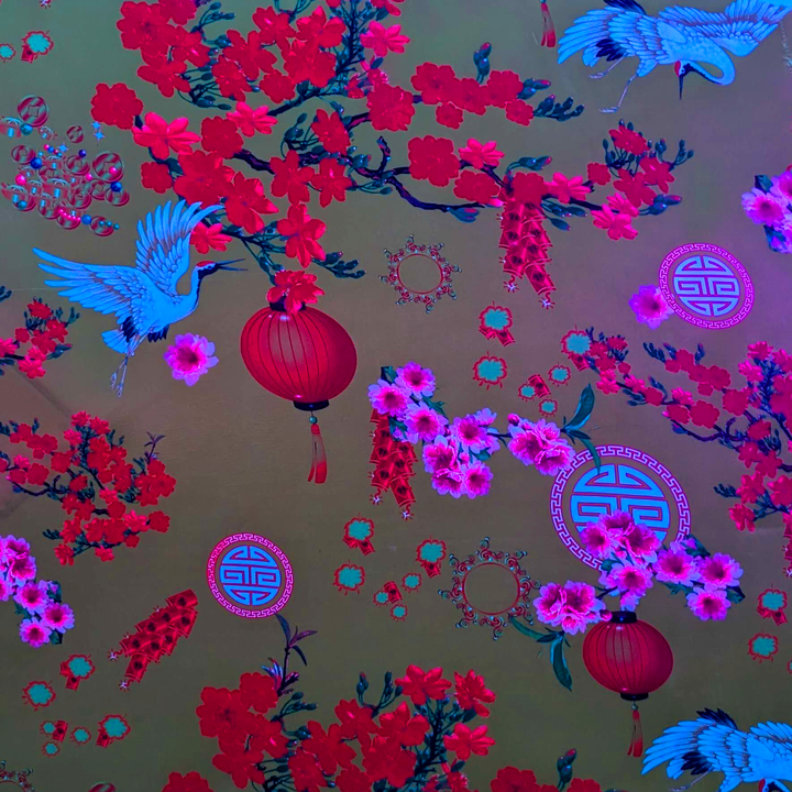 Close up of polyester silk fabric with a print of bright white birds, vibrant firecrackers, and pink and red blossoms lit under UV light.