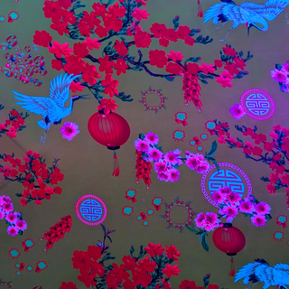 Close up of polyester silk fabric with a print of bright white birds, vibrant firecrackers, and pink and red blossoms lit under UV light.