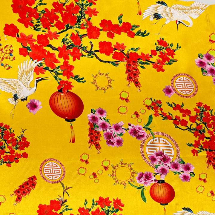 Close up of polyester silk fabric with a print of bright white birds, vibrant firecrackers, and pink and red blossoms lit under normal light.