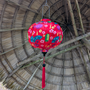 Red silk lantern with pink flowers, gold coins, fans and lanterns hanging against a thatched roof background