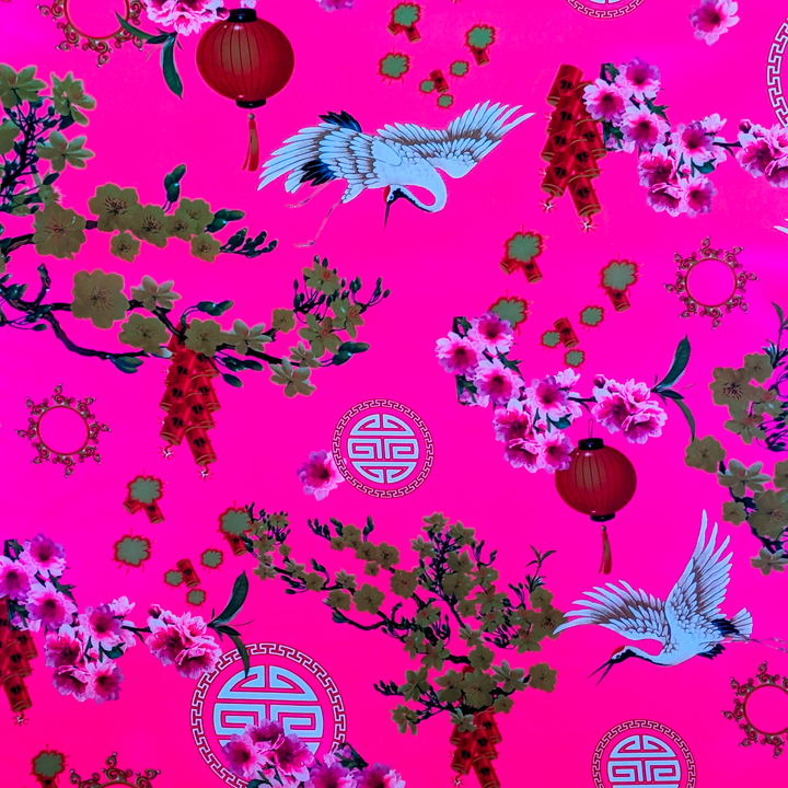 Close up of polyester silk fabric featuring cranes, lanterns, firecrackers, and blooms of pink and yellow on a brilliant pink background lit under UV light.