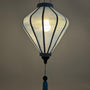A hanging light blue polyester linen lantern with a glowing bulb inside, featuring a blue tassel at the bottom