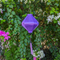Lozenge shaped light purple plain silk Hoi An Lantern hanging in front of plant with pink and white flowers.