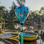 Balloon shape silk lantern with illustration of lotus flowers in full bloom against a vibrant turquoise-blue background hanging in front of basket boats on the river in Cam Thanh, Hoi An.